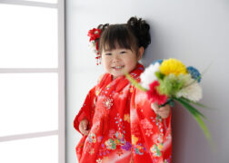 赤い被布で3歳の七五三写真撮影 花束を持って笑顔でポーズ