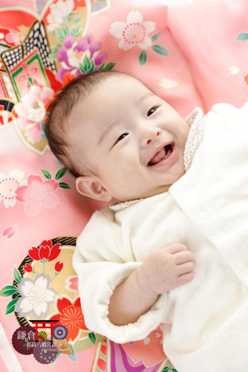 赤ちゃんのお宮参り記念写真撮影 ピンクの祝い着の上で笑顔の赤ちゃん