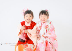 双子の女の子の七五三写真撮影 赤とピンクの被布で並んでポーズ