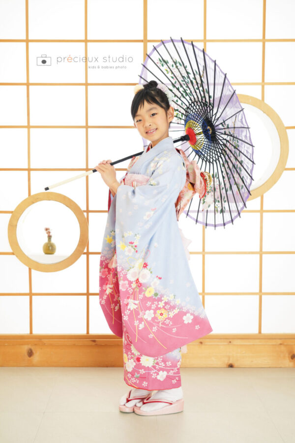 和傘を持って華やかな水色とピンクの着物で七五三写真撮影