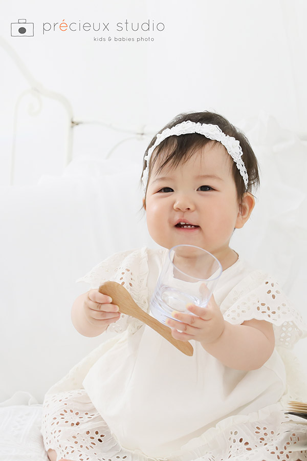 1歳のお誕生日記念写真の女の子 コップとスプーンを持ってにこにこ笑顔