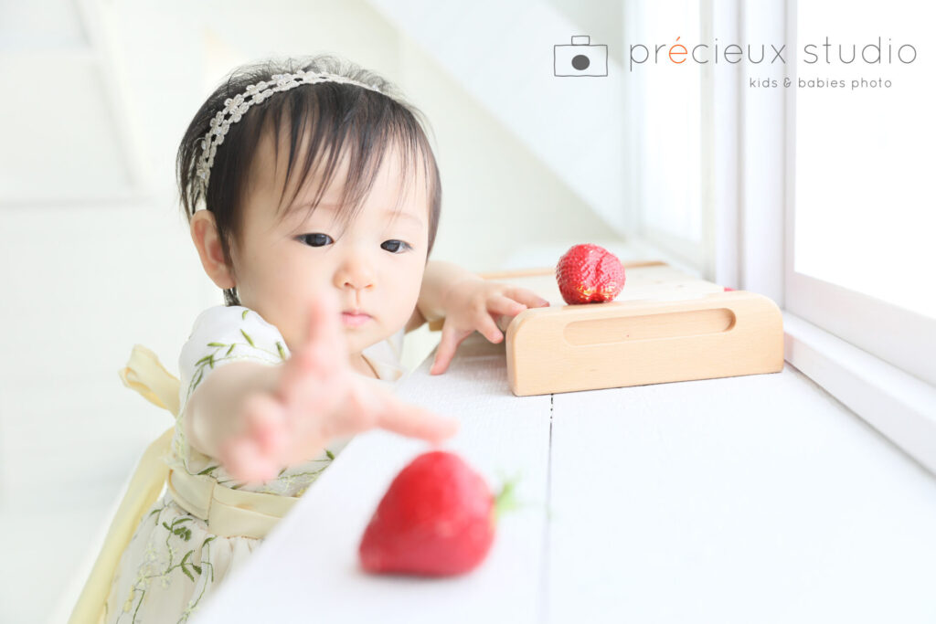 いちごに手を伸ばす1歳の女の子 スタジオでお誕生日記念写真撮影