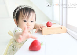 いちごに手を伸ばす1歳の女の子 スタジオでお誕生日記念写真撮影