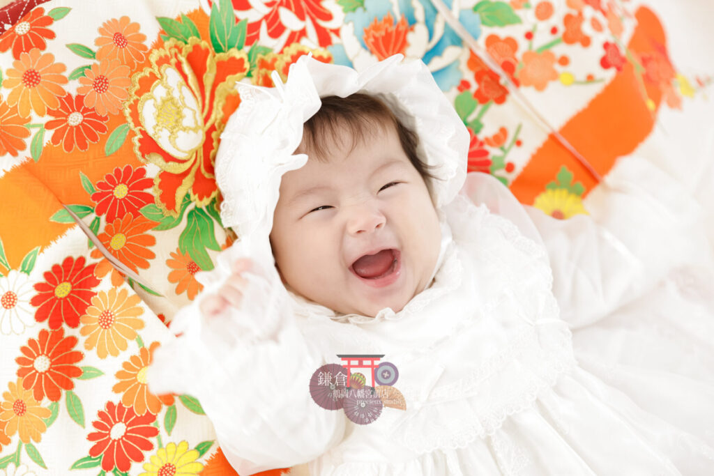 女の子のお宮参り記念写真撮影 オレンジの祝い着の上に寝転ぶベビードレスの赤ちゃん