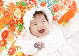 女の子のお宮参り記念写真撮影 オレンジの祝い着の上に寝転ぶベビードレスの赤ちゃん