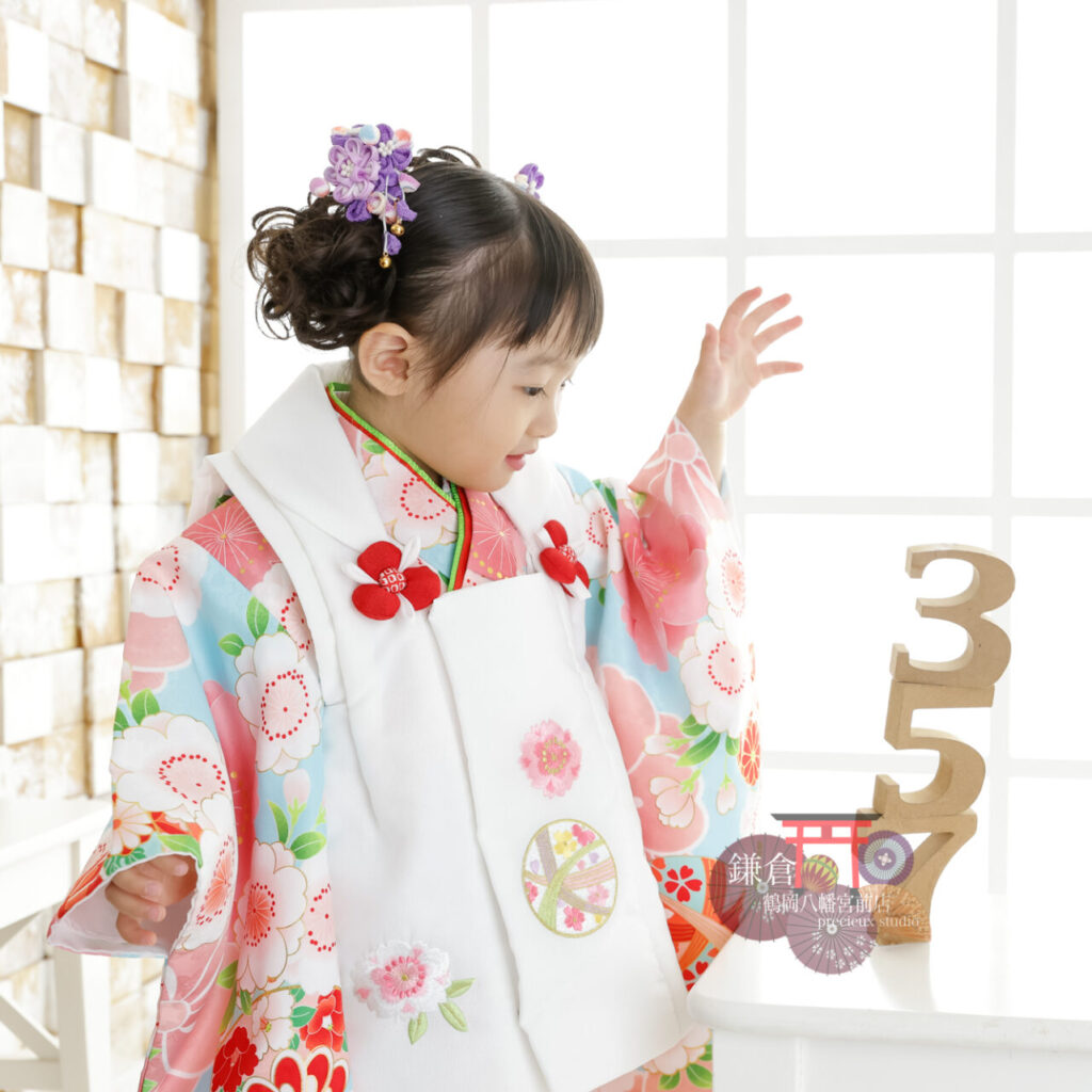 3歳の七五三記念写真撮影 白い被布にピンクと水色の着物の女の子 753のオブジェと一緒に
