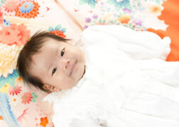 赤ちゃんのお宮参り記念写真撮影 ピンク・オレンジの掛け着に寝転ぶベビードレスの赤ちゃん