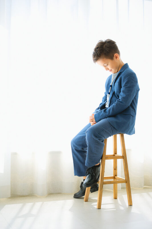 おしゃれなブルーのセットアップでハーフ成人式の記念写真撮影 座ってうつむきポーズの男の子