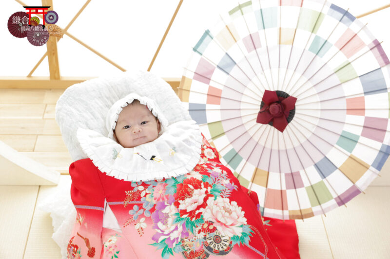 和室で赤ちゃんのお宮参り記念写真撮影 赤い掛け着・カラフルな和傘と一緒にスタジオ撮影の赤ちゃん