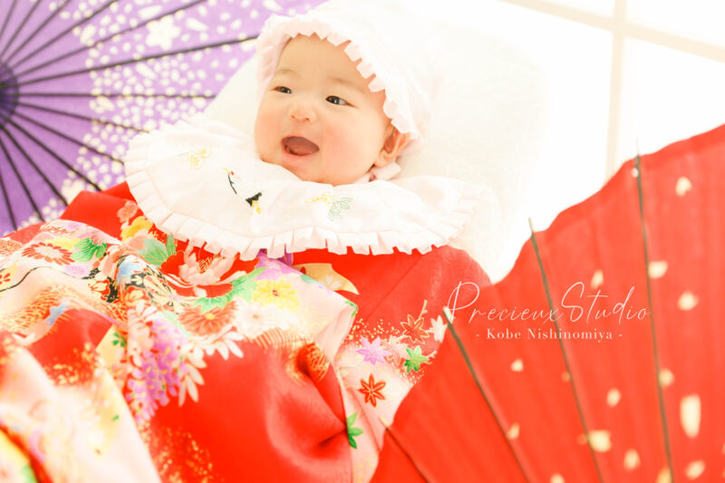 お宮参りの記念写真撮影 赤い掛け着と白い帽子とよだれかけの赤ちゃん