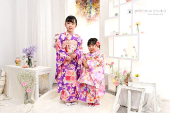 姉妹で七五三記念写真撮影 ピンクと紫の着物でお花に囲まれてポーズ