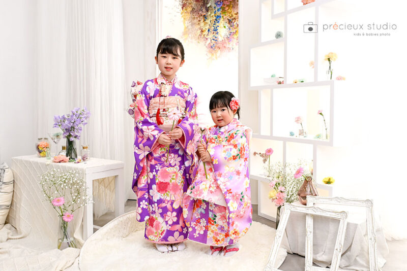 姉妹で七五三記念写真撮影 ピンクと紫の着物でお花に囲まれてポーズ