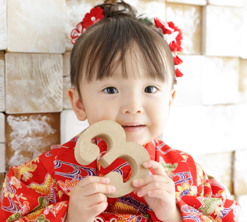 3のオブジェを持って3歳の七五三記念写真撮影 赤い着物の女の子