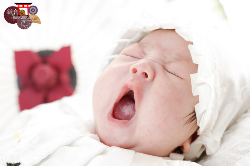 お宮参りの記念写真撮影であくびをする赤ちゃん 白い大黒帽子によだれかけで正装