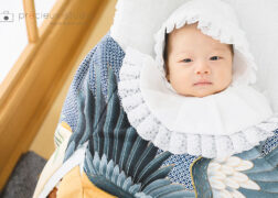 青みがかった産着と白いよだれかけ・帽子を身に着けたお宮参りの赤ちゃん