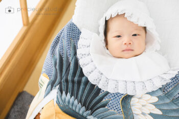 青みがかった産着と白いよだれかけ・帽子を身に着けたお宮参りの赤ちゃん