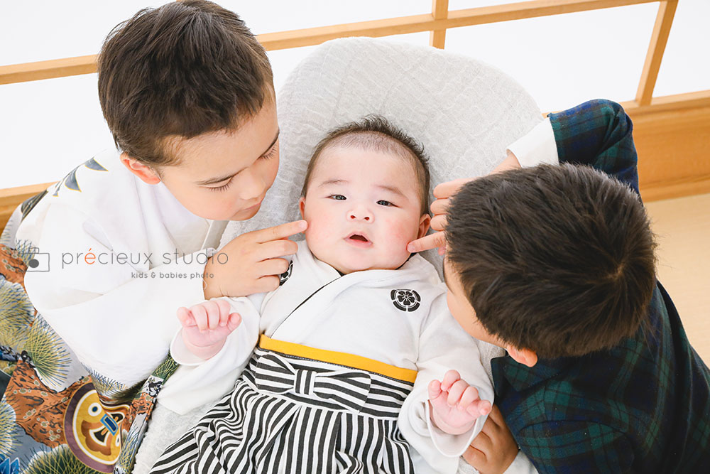 兄弟3人でお宮参りの記念写真撮影 弟のほっぺをつつくお兄ちゃんたち