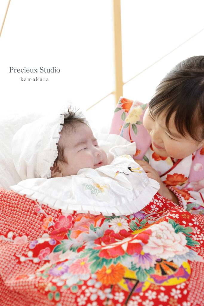 姉妹でお宮参りの記念写真撮影 赤い掛け着の妹とピンクの着物のお姉ちゃん